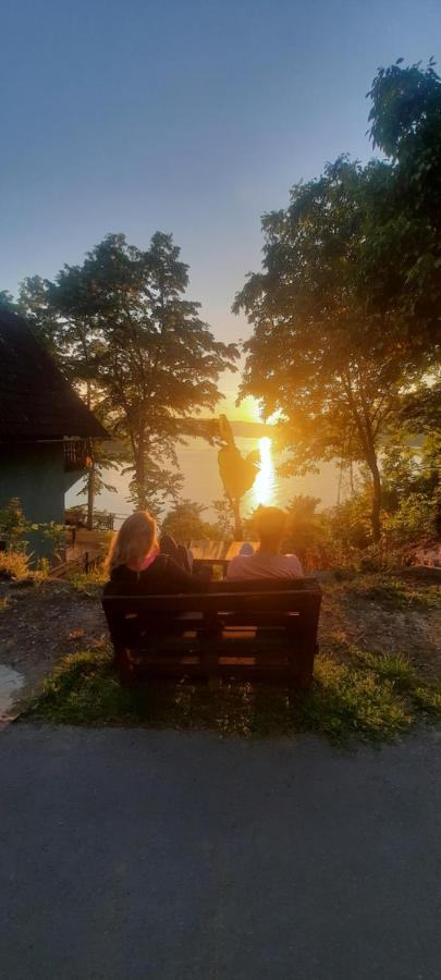 Two people on a bench in the garden, the sun setting over the river in front of them