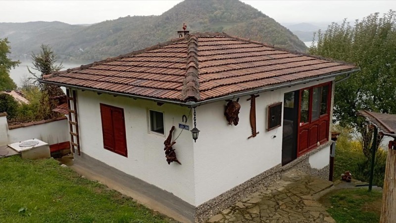The whitewashed house with a tiled roof and red shutters, behind it the Danube and the hills of Đerdap