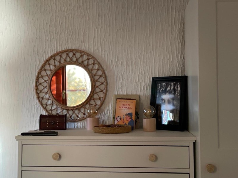 White chest of drawers with a round rattan mirror, a picture frame and a lamp